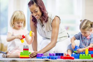 Teacher assisting young students building with plastic blocks